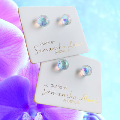 A pair of  world class Samantha Abbott glass earrings on branded display cards with a purple orchid in the background